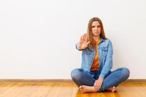Woman in denim sitting on wooden floor showing stop gesture photo