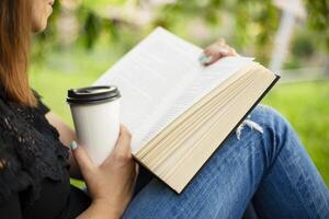 mujer leyendo libro y participación café taza en parque. foto