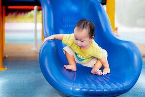 Portrait of a 1 year and 5 month old Asian boy having fun playing on a blue slide at outdoor playground. Toddlers are learning new things. Baby children and the development of large and small muscles. photo