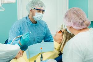 The patient smiles in the dentist's chair in a protective mask and instrument before treatment in the dental office photo