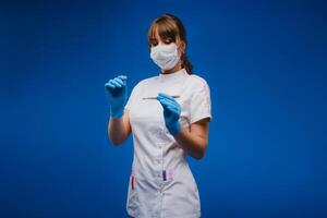 An attractive young female doctor holds a scalpel and looks directly at the camera. Concept of healthcare, treatment and surgery. Portrait of a medical practitioner on a blue background photo