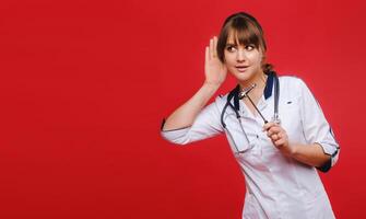 A doctor in a white coat on a red background holds a neurological hammer and listens to something photo