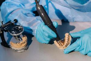 A masked and gloved dental technician works on a prosthetic tooth in his lab photo
