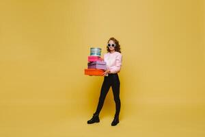 A happy young woman with colorful paper boxes after shopping isolated on an orange Studio background. Seasonal sales, purchases, spending money on gifts photo