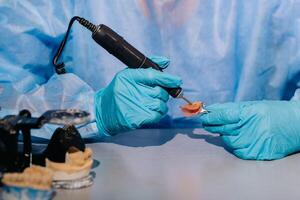 A masked and gloved dental technician works on a prosthetic tooth in his lab photo