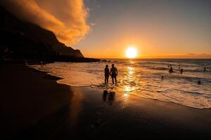 A couple in love stands in the ocean in the evening looking at the beautiful sunset on the island of Tenerife.Spain photo