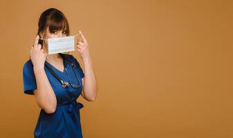 A girl doctor stands in a medical mask, isolated on a brown background photo