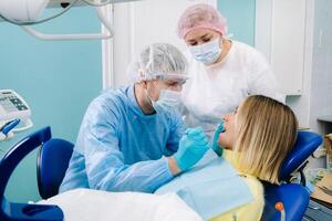 The patient smiles in the dentist's chair in a protective mask and instrument before treatment in the dental office photo