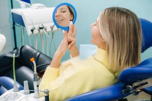 el niña sonrisas y mira en el espejo en el del dentista oficina foto