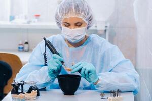 A dental technician in protective clothing is working on a prosthetic tooth in his laboratory photo