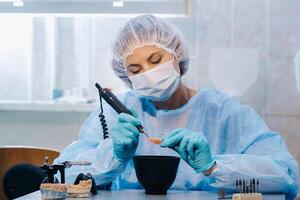 A dental technician in protective clothing is working on a prosthetic tooth in his laboratory photo