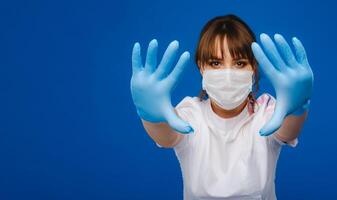 A girl doctor stands in a medical mask and gloves on an isolated blue background photo