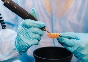 A masked and gloved dental technician works on a prosthetic tooth in his lab photo