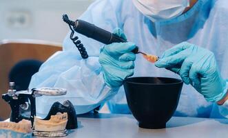 A masked and gloved dental technician works on a prosthetic tooth in his lab photo