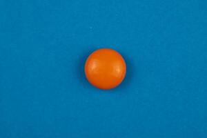 Round orange pill or drug isolated on blue background in macro view. photo