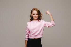 A beautiful girl on a gray background shows the strength of her biceps. photo