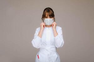 A girl doctor stands in a medical mask, isolated on a gray background. photo