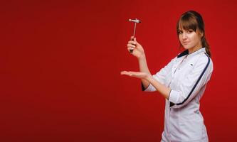 A doctor in a white coat holds a neurological hammer on a red background to test reflexes photo