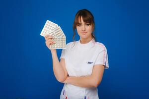 The concept of health care. A young brunette doctor in a white coat on a blue background shows plates with capsules to take. photo