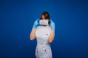 un médico niña soportes en un médico máscara en un aislado azul antecedentes foto