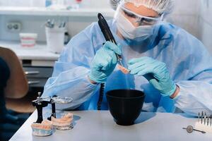 A masked and gloved dental technician works on a prosthetic tooth in his lab photo