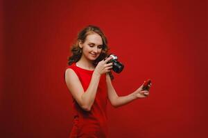 un sonriente joven mujer con ondulado pelo sostiene un fresa y fotografias él, participación un delicioso Fresco fresa en un brillante rojo antecedentes foto