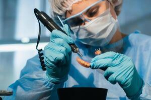 A masked and gloved dental technician works on a prosthetic tooth in his lab photo