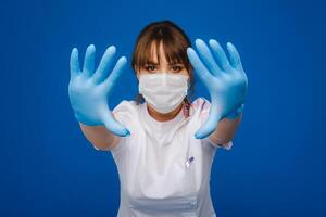 A girl doctor stands in a medical mask and gloves on an isolated blue background photo