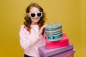 A happy young woman with colorful paper boxes after shopping isolated on an orange Studio background. Seasonal sales, purchases, spending money on gifts photo