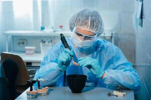 A masked and gloved dental technician works on a prosthetic tooth in his lab photo