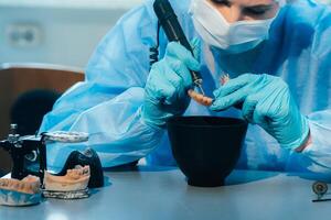 A masked and gloved dental technician works on a prosthetic tooth in his lab photo