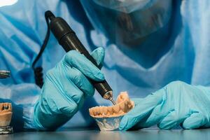 A masked and gloved dental technician works on a prosthetic tooth in his lab photo