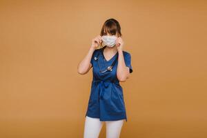 A girl doctor stands in a medical mask, isolated on a brown background photo