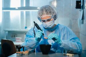 A masked and gloved dental technician works on a prosthetic tooth in his lab photo