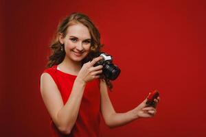 a smiling young woman with wavy hair holds a strawberry and photographs it, holding a delicious fresh strawberry on a bright red background photo