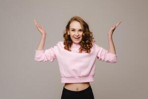 A beautiful emotional girl raises her hands up from happiness and what she sees on a gray background photo