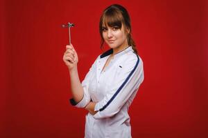 The doctor is holding a neurological hammer on a red background. The neurologist checks the patient's reflexes with a hammer. Diagnostics, healthcare, and medical care photo