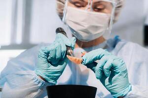 A masked and gloved dental technician works on a prosthetic tooth in his lab photo