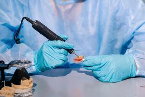 A masked and gloved dental technician works on a prosthetic tooth in his lab photo