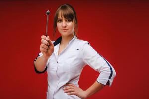 The doctor is holding a neurological hammer on a red background. The neurologist checks the patient's reflexes with a hammer. Diagnostics, healthcare, and medical care photo