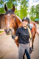 Lovely young woman wearing helmet stroking to her brown horse photo