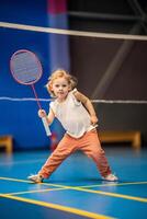 pequeño niña Tres años antiguo jugando bádminton en deporte vestir en interior Corte foto