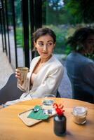 joven negocio mujer participación y Bebiendo café en calle café en ciudad. retrato de hermosa mujer trabajador esperando cliente en calle de Praga foto