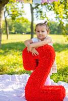 Cheerful girl having fun on child birthday on blanket with paper decorations in the park photo