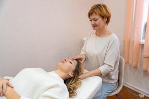 Healer woman performing by lightly touched set of 32 points of access bars on young woman head, stimulating positive change thoughts and emotions in salon. Alternative medicine concept photo