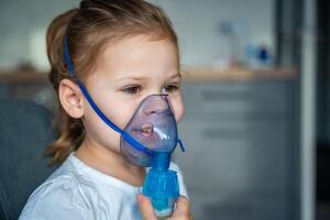 Cute little girl are sitting and holding a nebulizer mask leaning against the face, airway treatment concept photo