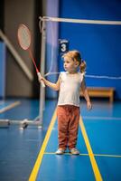 pequeño niña Tres años antiguo jugando bádminton en deporte vestir en interior Corte foto