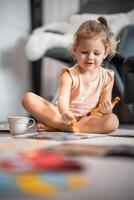 Little girl sits on the floor at home and draws with paints and brushes in a coloring book. Early childhood creativity and education photo