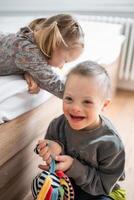 pequeño chico con abajo síndrome obras de teatro con su mas joven hermana en el cama en hogar dormitorio. alto calidad foto