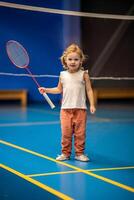 pequeño niña Tres años antiguo jugando bádminton en deporte vestir en interior Corte foto
